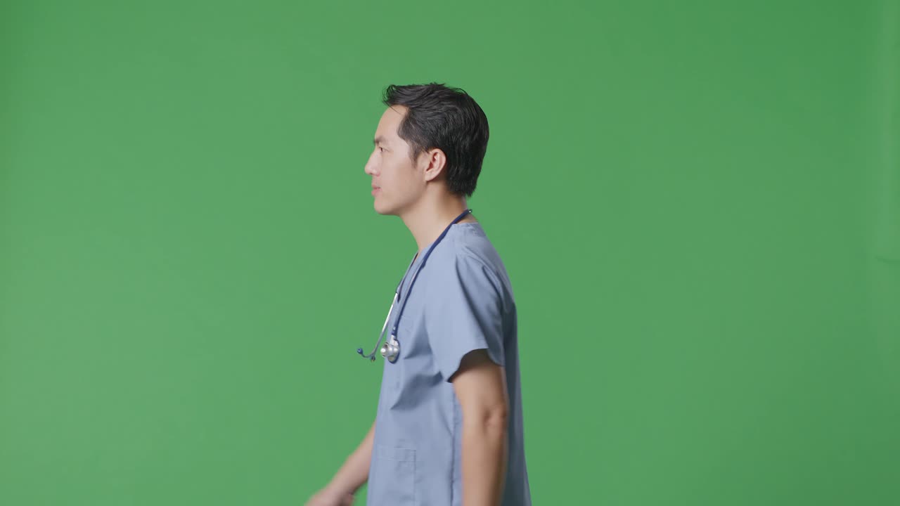 Side View Of Asian Male Doctor With Stethoscope Walking On Green Screen Background In The Hospital