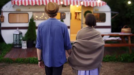 Romantic-Couple-Living-Or-Having-Vacation-In-Trailer-Girl-Covered-With-Brown-Plaid-Walking-With-Her-Man-Inside-To-The-Trailer,-Holding-Hands