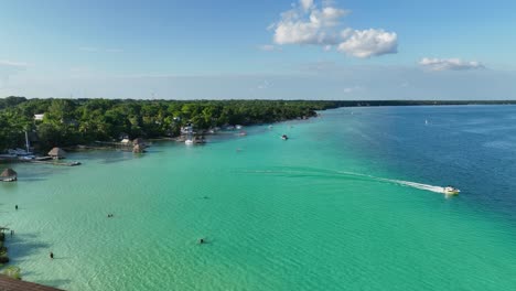 aerial view boat leaving the bacalar town, in sunny mexico - static, drone shot