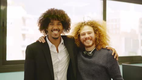 Coworkers with curly hair embracing in the office
