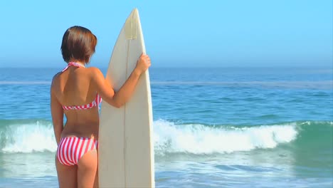 woman holding her surfboard looking at the sea