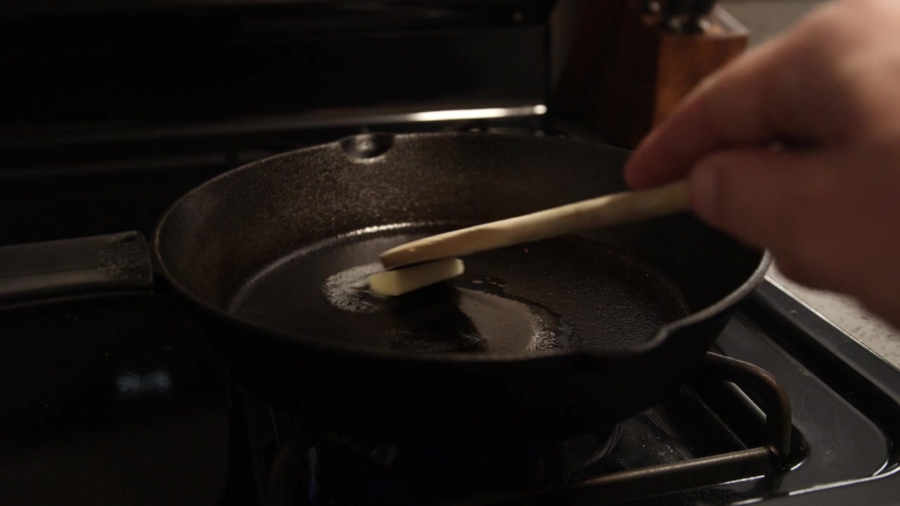 Butter frying in a cast iron skillet on a gas stove. Hand with wooden spoon in a pan