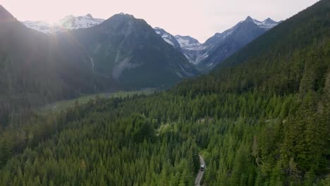 duffey lake road with traveling vehicle in the midst of dense thicket and snow mountains background in pemberton, bc canada