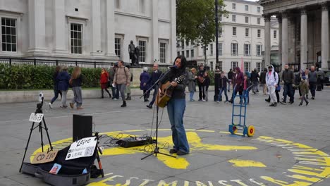 street musician playing guitar and singing for a crowd in trafalgar square, london