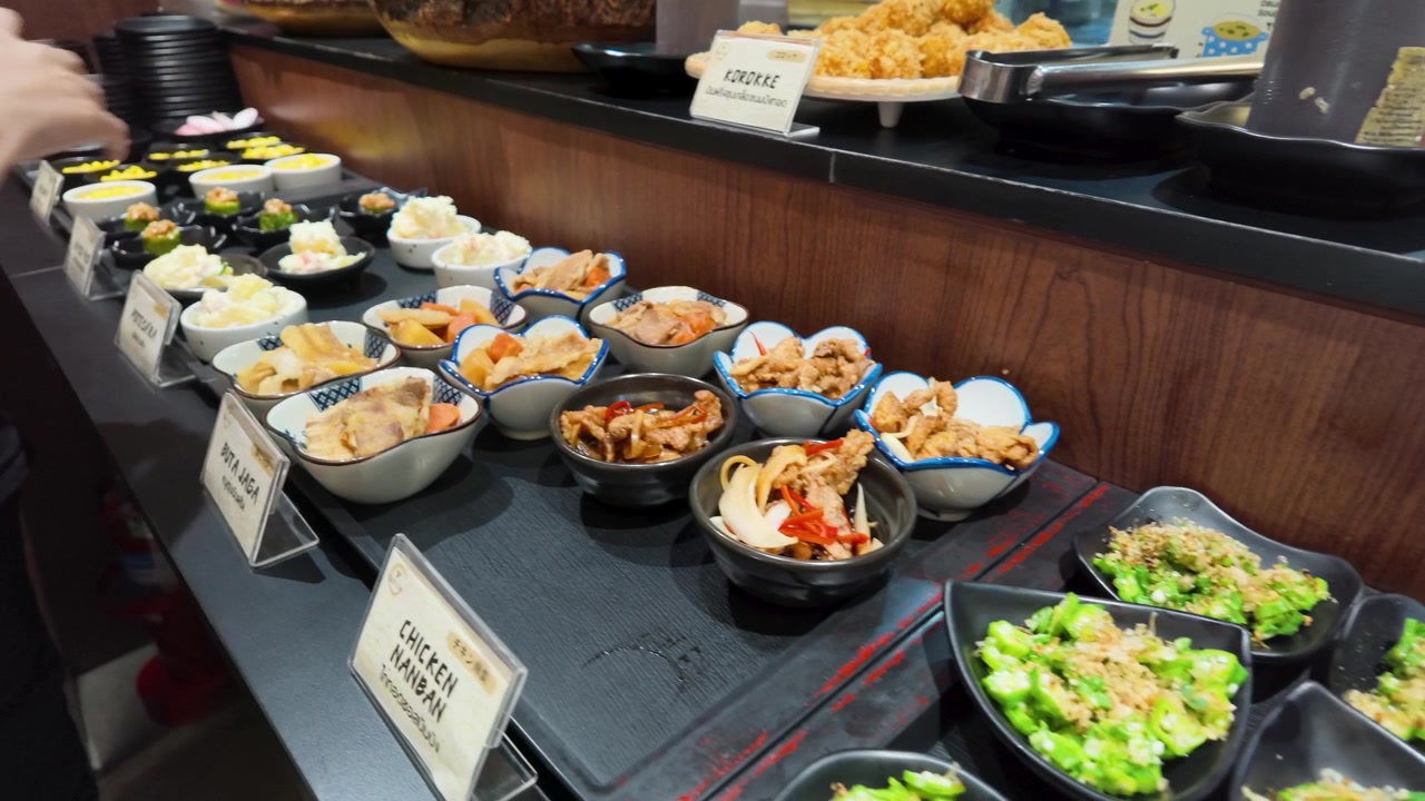 Una mano prende piccole ciotole di cucina giapponese da un vario banco buffet a Bangkok