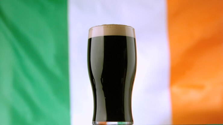 Una pinta di stout irlandese sullo sfondo di una bandiera irlandese che sventola