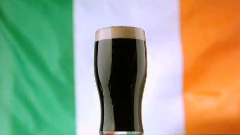 de una pinta de stout irlandés en el fondo de la bandera irlandesa ondeando