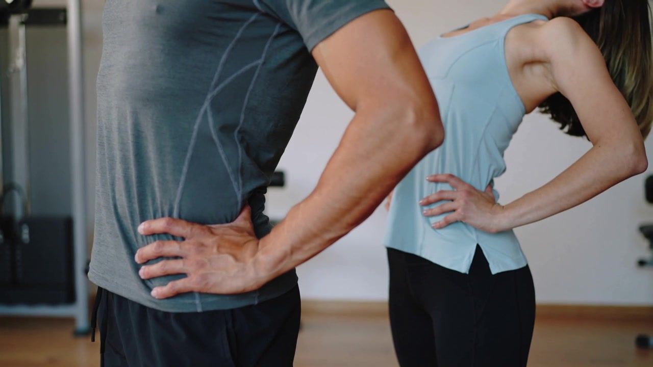 Starting upright hands on hips, pair performing backbend for mobility in gym, grey blue tops, cable