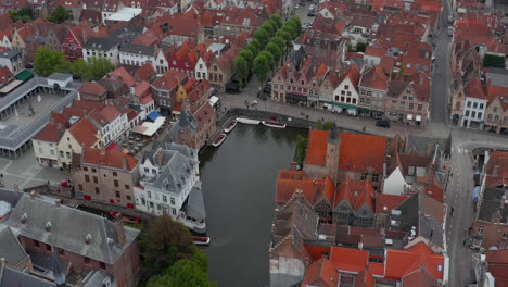 Bruges,-Belgium-Cityscape-with-River-and-Boats,-Aerial-tilt-down