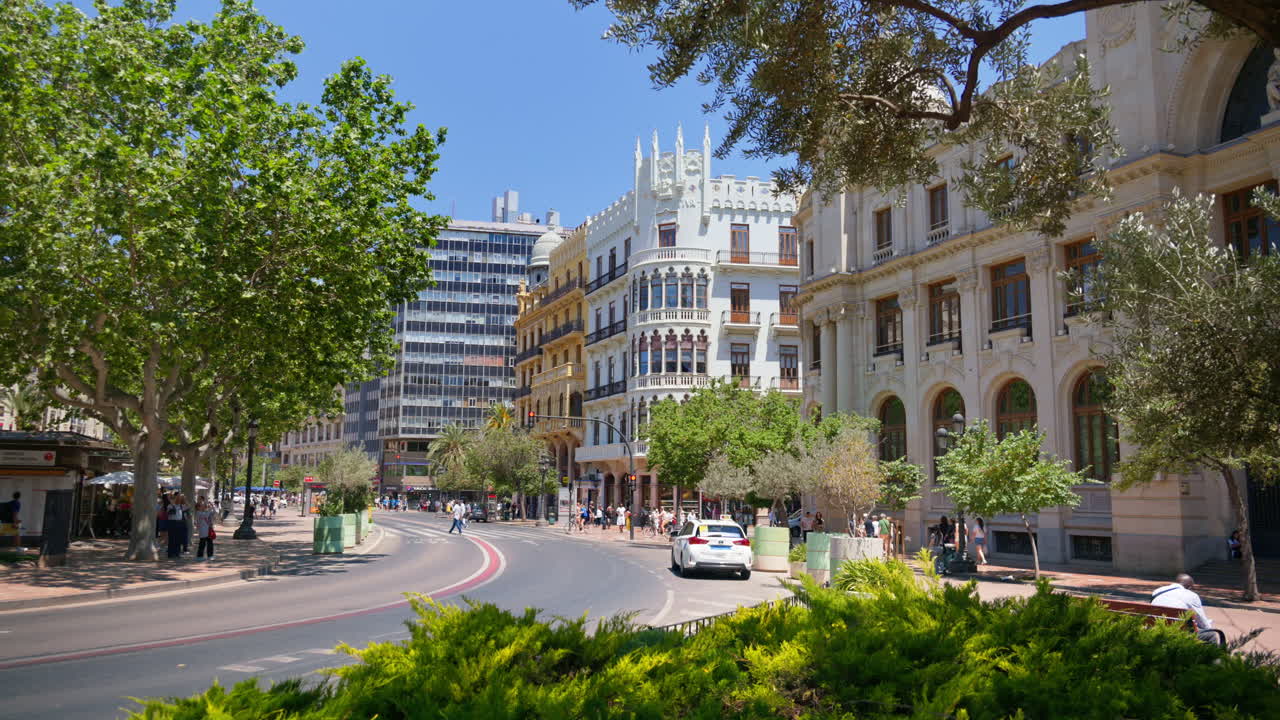 Valencia, Spain - May 29, 2025: Traffic and pedestrians along the curved avenue edging Plaza del Ayuntamiento, mixing modern and historic facades with street greenery