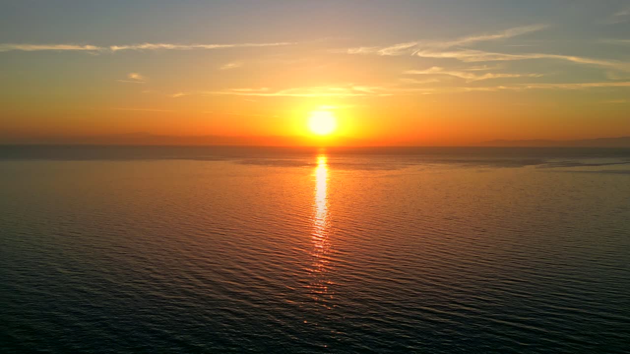 Tilt up aerial shot of a stunning sunset in Greece over the ocean, a distant island on the horizon.