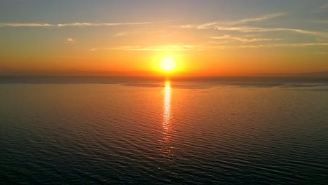 tilt up aerial shot of a stunning sunset in greece over the ocean, a distant island on the horizon.