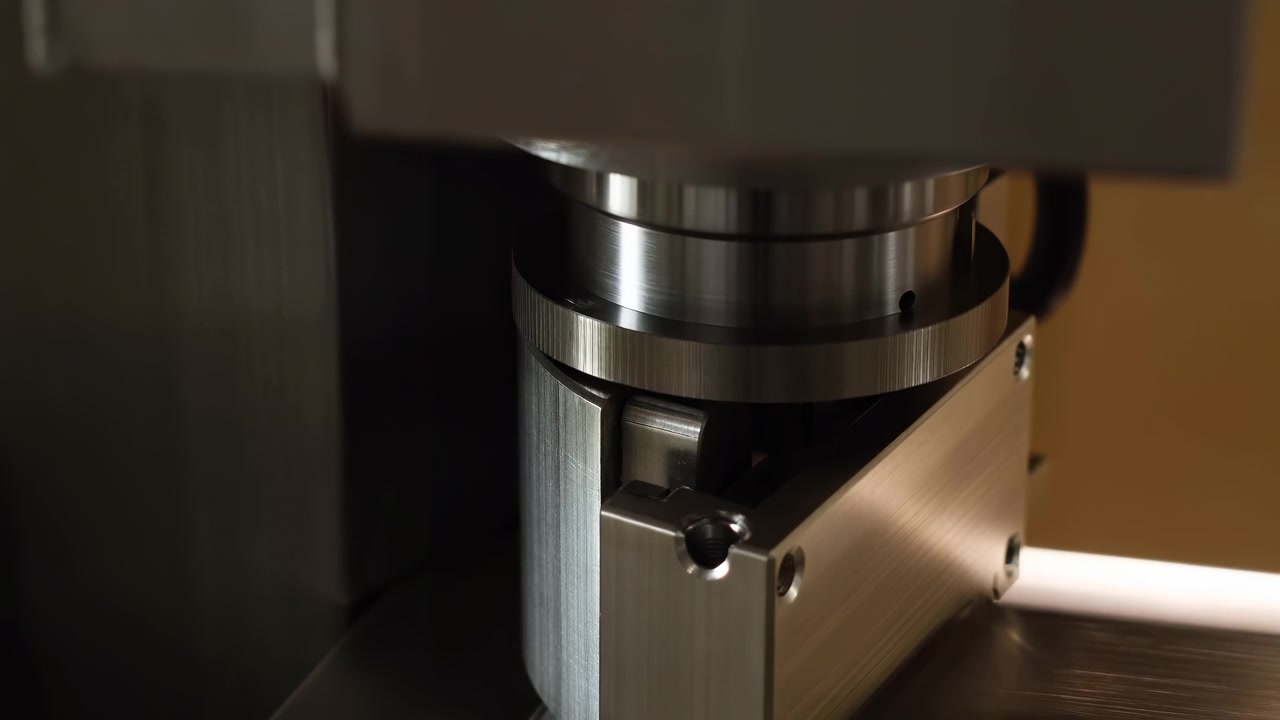 Nærbilde viser en metallmekanisme som beveger seg inne i kompakt utstyr, med reflekterende overflater, mørke omgivelser og fokusert belysning som fremhever presisjonsstruktur og industrielle detaljer.