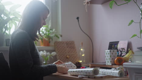young beautiful white girl packing gift items with white decorative paper for celebrating an event