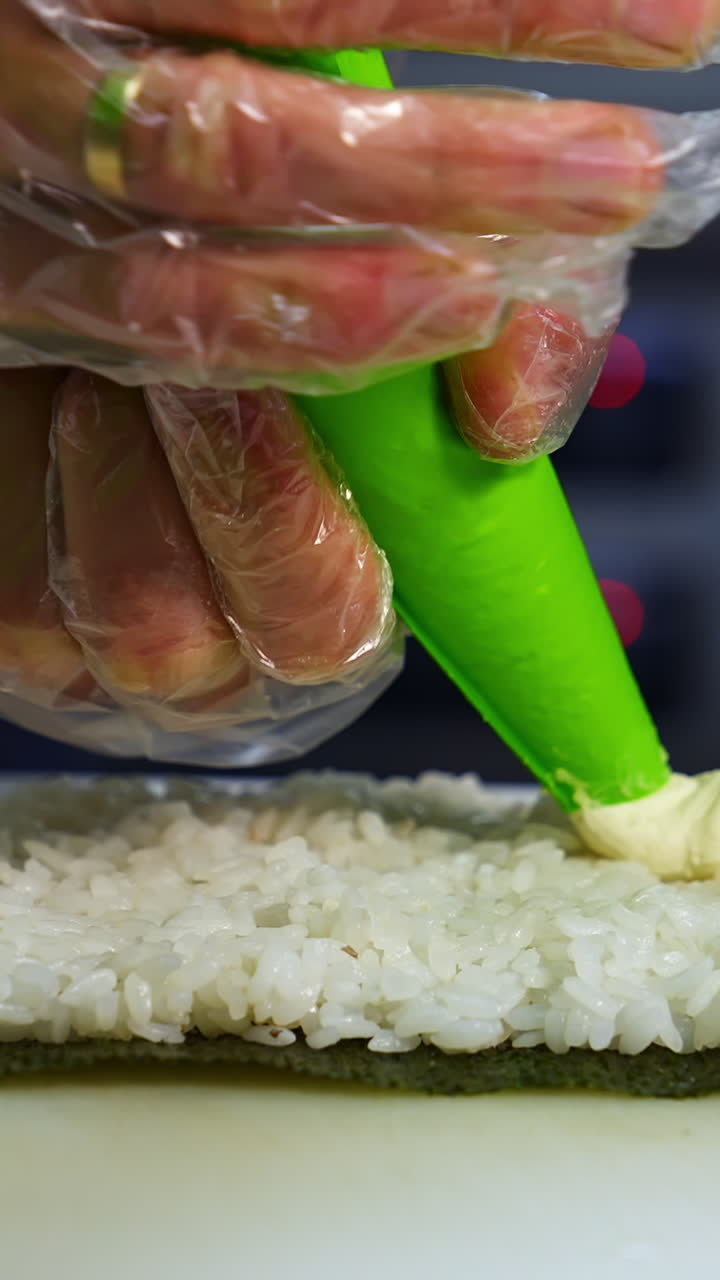Chef in restaurant prepares sushi rolls with tasty ingredients. Cook`s hands putting cream cheese. Delicious asian food concept. Vertical video