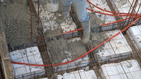 Close-up-of-the-legs-of-a-construction-worker-wearing-boots-applying-concrete-mix-on-the-grid-mesh-of-a-new-house-flooring-using-a-boom-pump-in-Mexico