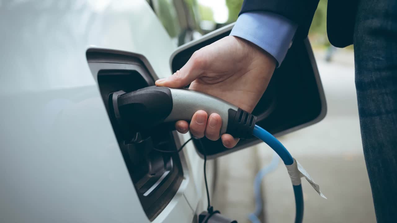 Elektrikli arabayı şarj eden beyaz erkeğin orta bölümü.