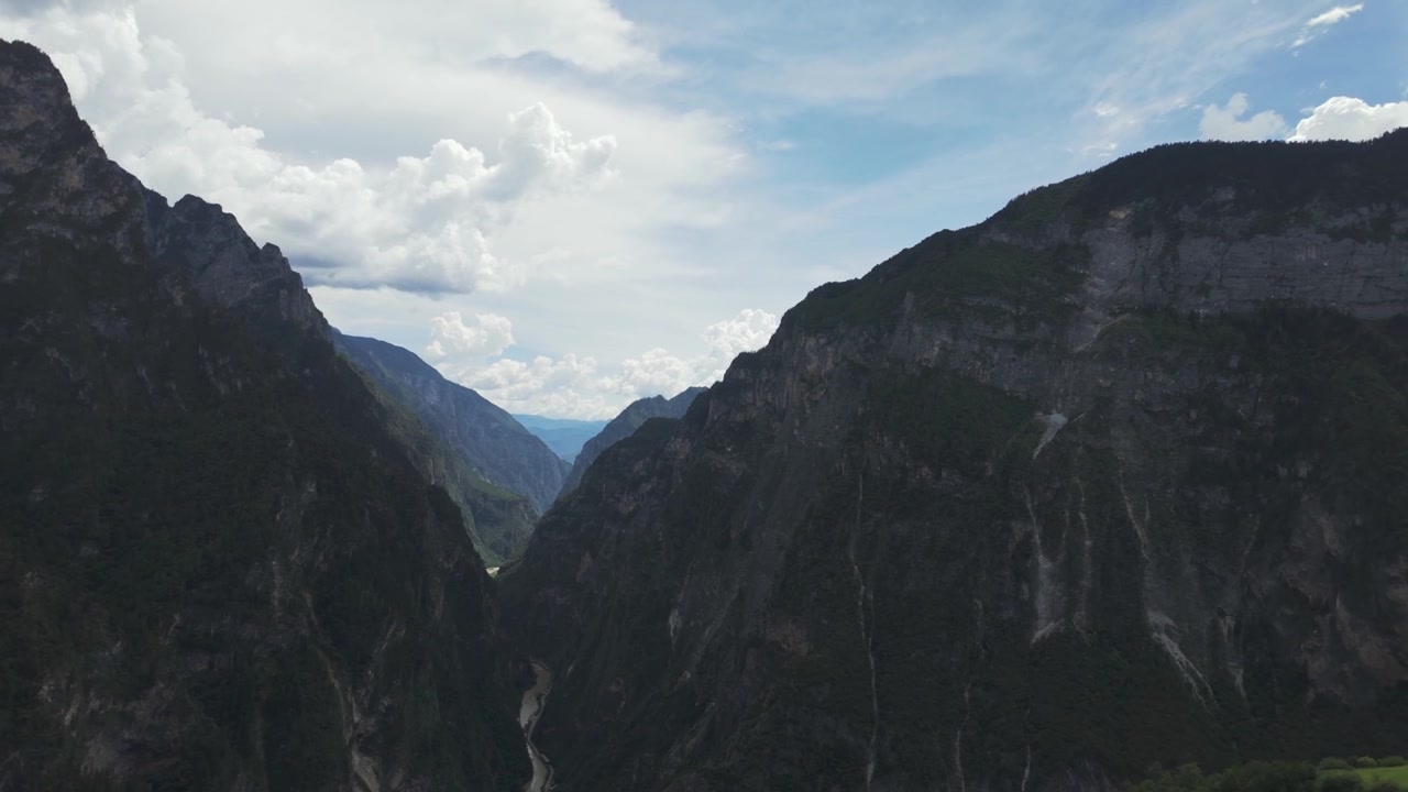 Sebuah bidikan udara sinematik yang dramatis terbang melalui ngarai gunung yang dalam dengan tebing berbatu curam di bawah langit berawan. Menangkap skala dan keindahan alam yang mentah.