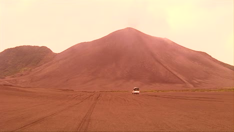 Un-Vehículo-Circula-A-Través-De-Un-Paisaje-Desértico-Mientras-Se-Forma-Una-Nube-De-Ceniza-Volcánica-En-El-Fondo