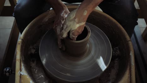 hands of a young male potter working on a potter's wheel and making a pot