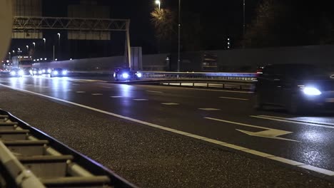 Stadtverkehr---Eine-Stetige-Aufnahme-Von-Vorbeifahrenden-Autos,-Die-Nachts-Von-Einer-Stark-Befahrenen-Autobahn-In-Die-Stadt-Kommen