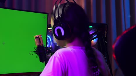 close up back view of asian girl streamer stretching after using green screen personal computer. live stream on desk illuminated by rgb led strip light