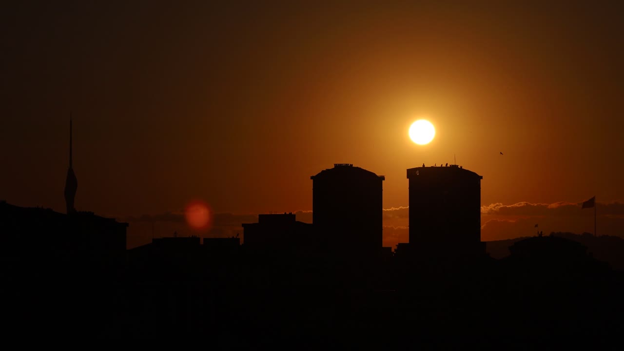 Sol poniéndose bajo las nubes, fundido a negro contra siluetas de edificios, espacio para texto