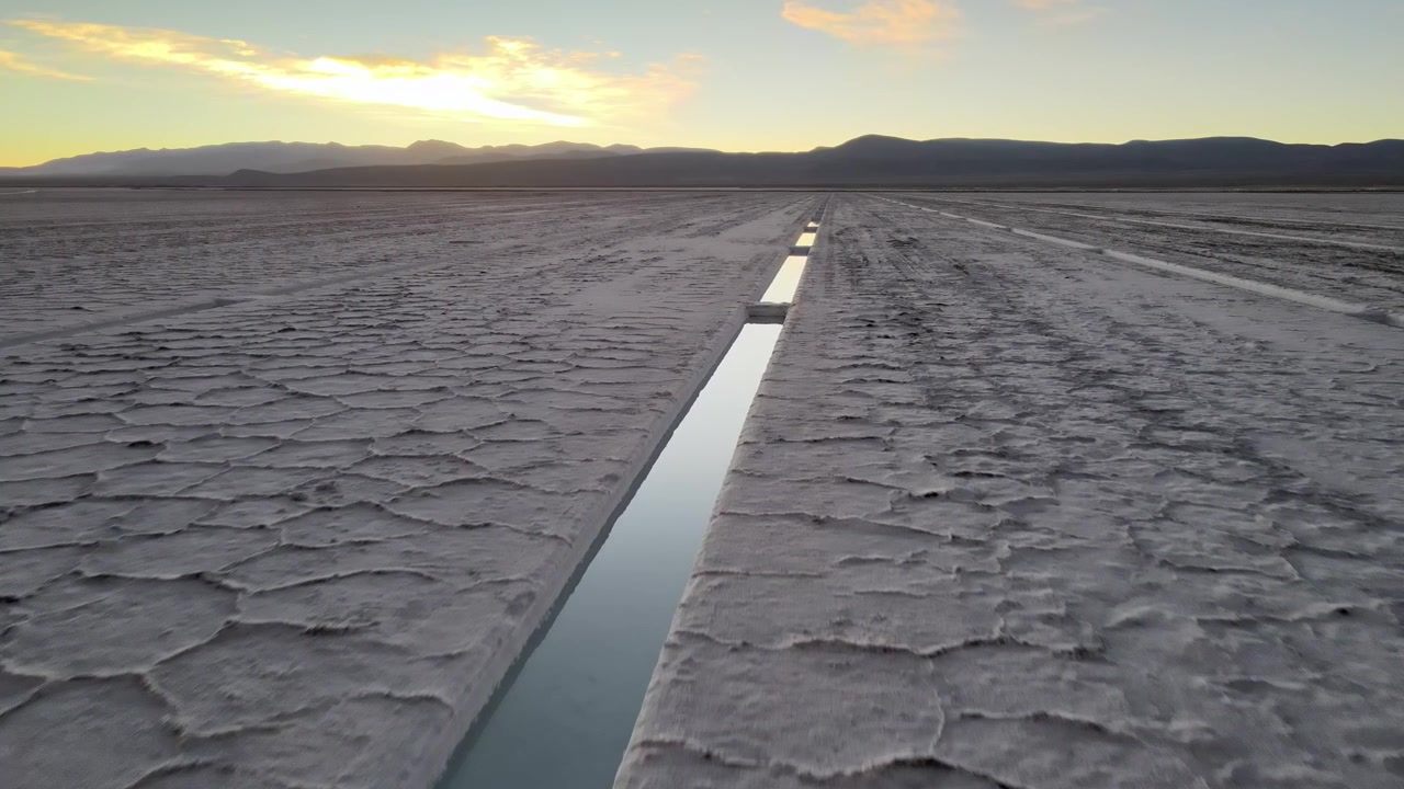 Narrow reflective drainage channel cuts through cracked salt crust of Salinas Grandes salt flat at sunrise in Jujuy, Argentina.