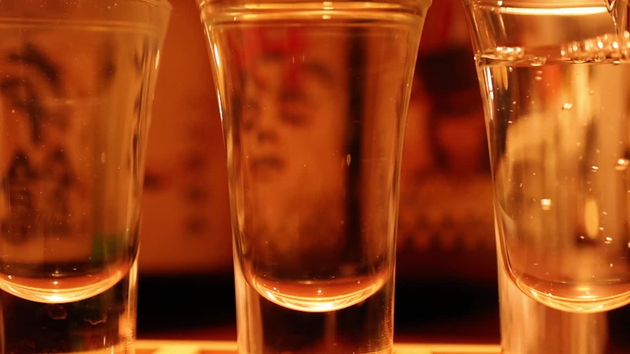 Una sequenza ravvicinata che mostra un liquido trasparente che riempie dei piccoli bicchieri di vetro sul bancone di un bar