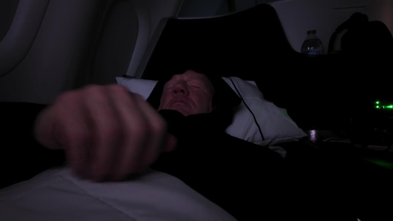 Close Up Shot Of A Senior Man In First Class On A Commercial Flight Trying To Sleep During Turbulence