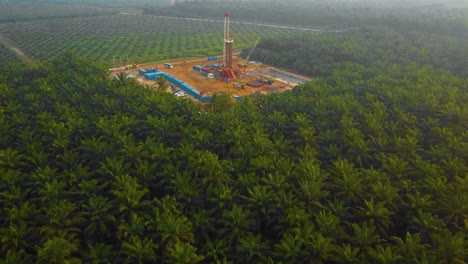 Cinematic-Drone-Shot-of-Onshore-Drilling-and-Workover-Rig-structure-and-Rig-equipment-for-oil-exploration-and-exploitation-in-the-middle-of-jungle-surrounded-by-palm-oil-trees-during-sunset-time