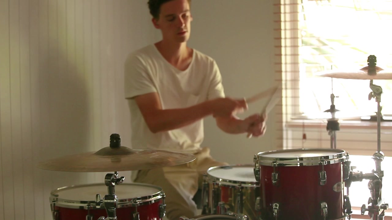Wide shot of drummer holding down a beat on home drum kit with natural light casting perfect shadow behind.
