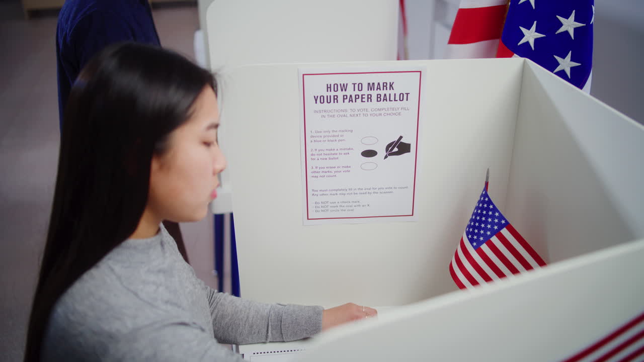 Asian Female Voter with Ballot Comes to Voting Booth and Votes Asian Female Voter with Ballot Comes to Voting Booth at Polling Station Makes Choice and Votes for Presidential Candidate us Citizen during National Election Day in the United States of America