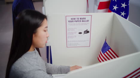 asian female voter with ballot comes to voting booth and votes asian female voter with ballot comes to voting booth at polling station makes choice and votes for presidential candidate us citizen during national election day in the united states of america