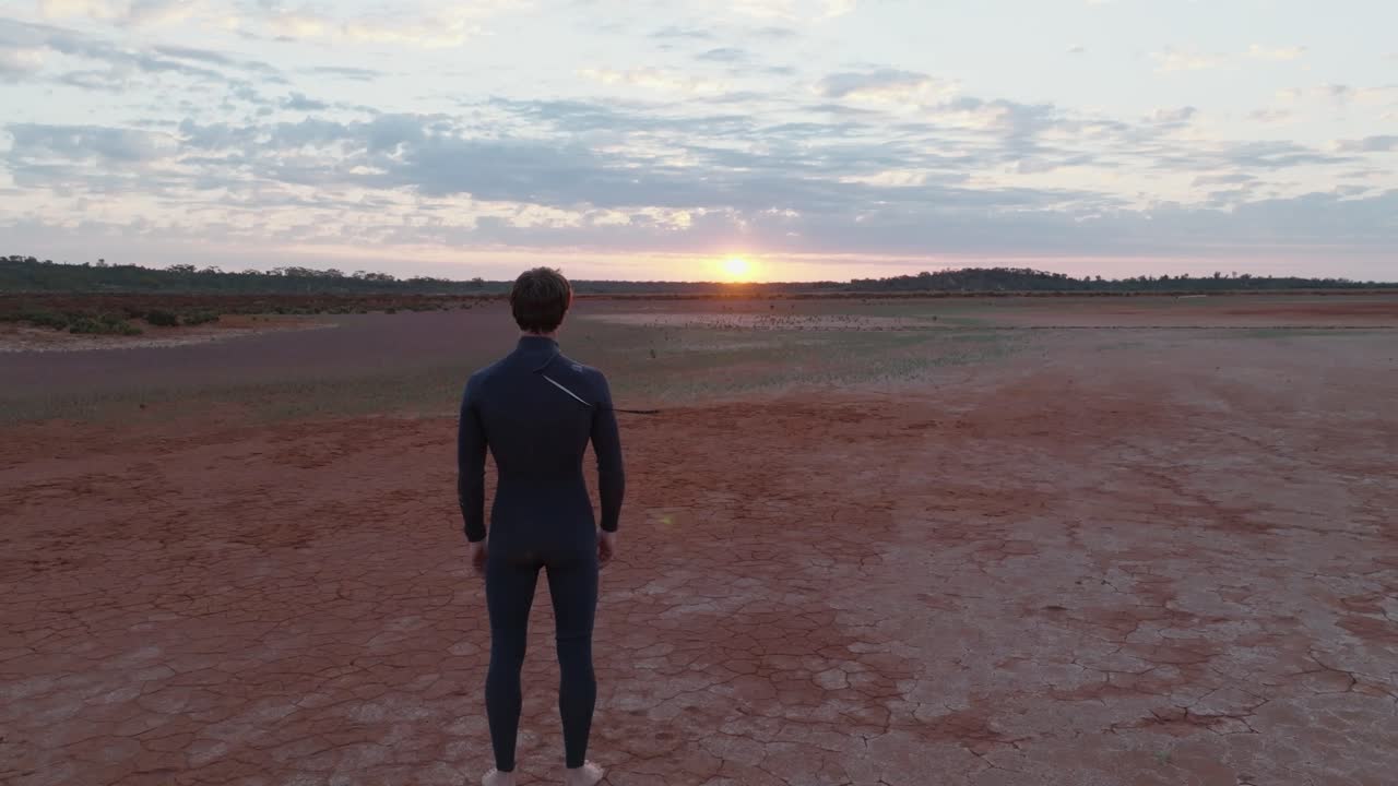 Male model wearing wetsuit, looking at camera then turning round to look towards sunrise