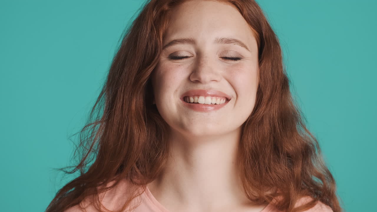 Redheaded girl looking at camera on turquoise background.