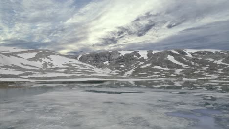 statuesque norwegian mountains are set between cold fjord waters, reflecting the heaven above, and the dense sky immensely inhabited with floating in different directions grey, white, and blue clouds