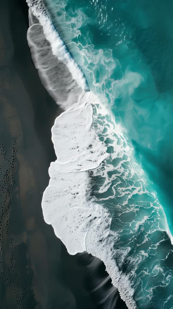 Vista aerea di onde che si infrangono su una spiaggia sabbiosa scura, creando uno splendido contrasto