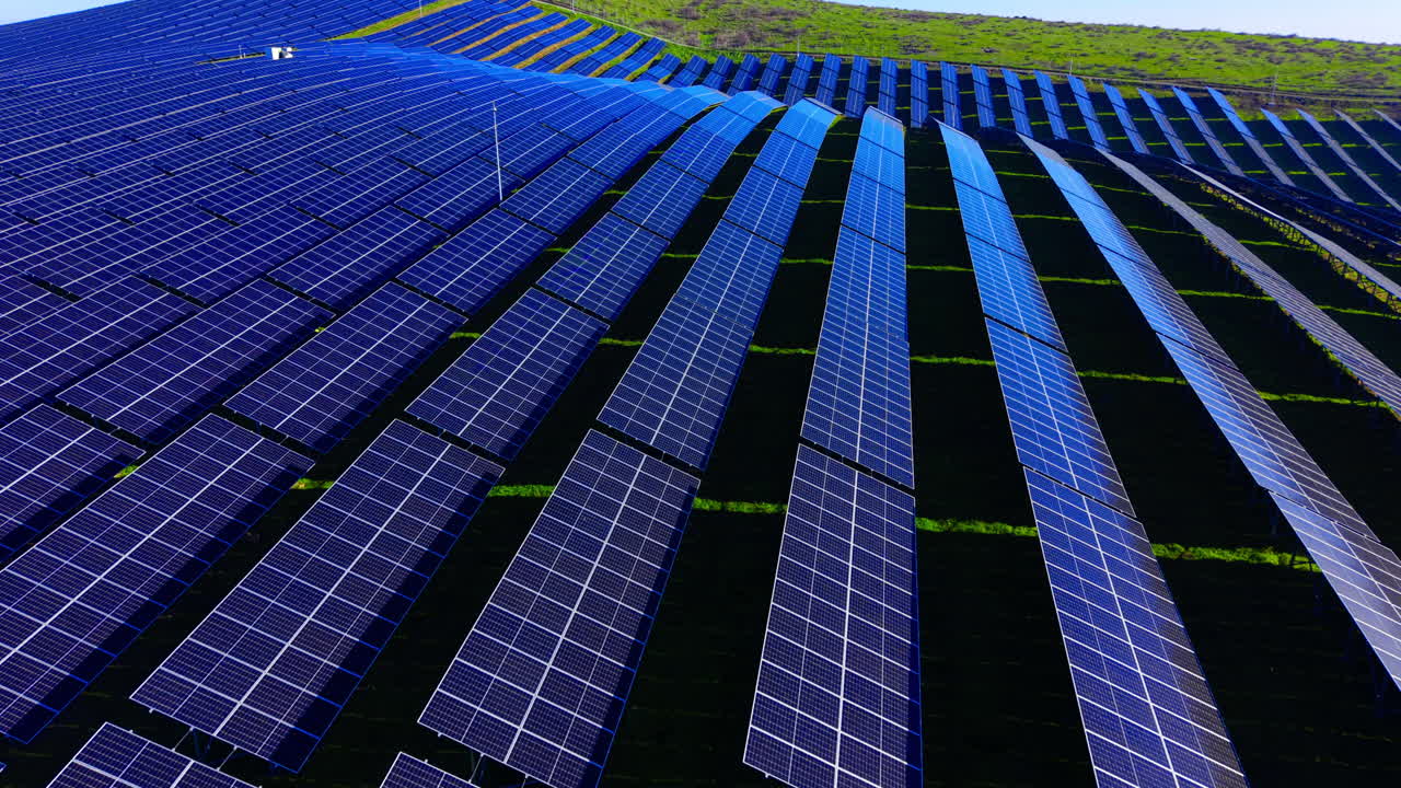 Una ripresa aerea prospettica che mette in evidenza le file ritmiche e le ombre dei pannelli solari fotovoltaici su un pendio verde naturale