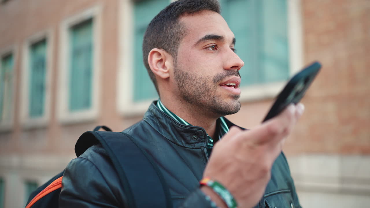 Young man recording a voice message on smartphone outdoors.