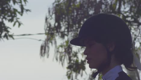 face profile of pretty woman equestrian riding horse outdoors - tracking shot against sky and tree branches