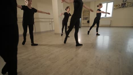 a group of young ballet students in black dancewear practicing positions in a spacious ballet studio with wooden flooring and wall-mounted barres. focused expressions and synchronized movements.