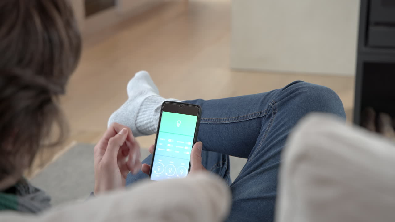 Relaxing at home, person using smartphone to control smart home lighting