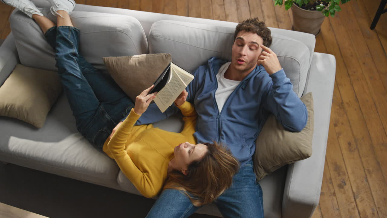Young spouses reading book comfortable couch top view. Couple talking together