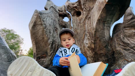 beautiful baby boy focused on the book turning pages. kid sits outdoors on the wooden throne. low angle view.