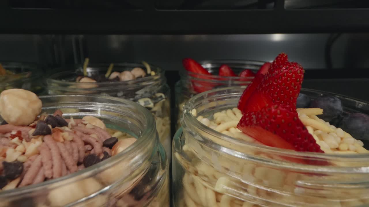 Jars of delicious spaghetti ice cream with toppings strawberries and raspberries placed in fridge section.
