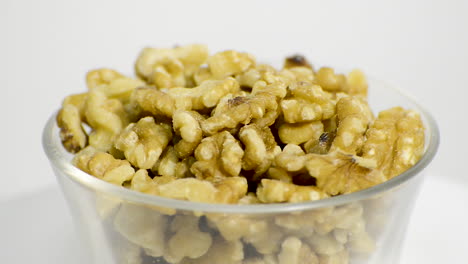 tazón de vidrio transparente con mitades de nueces sin cáscara girando sobre un fondo blanco