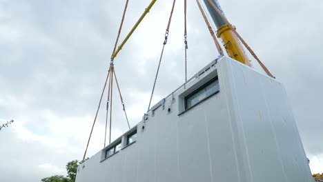 grua industrial pesada levantando parte de una casa modular, vista desde abajo