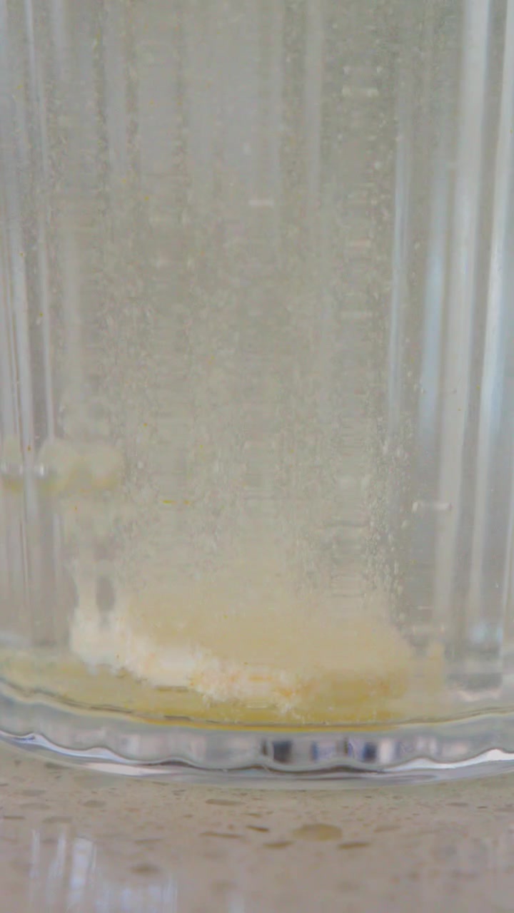 Primo piano di una compressa effervescente bianca che si dissolve con bollicine in un bicchiere d'acqua