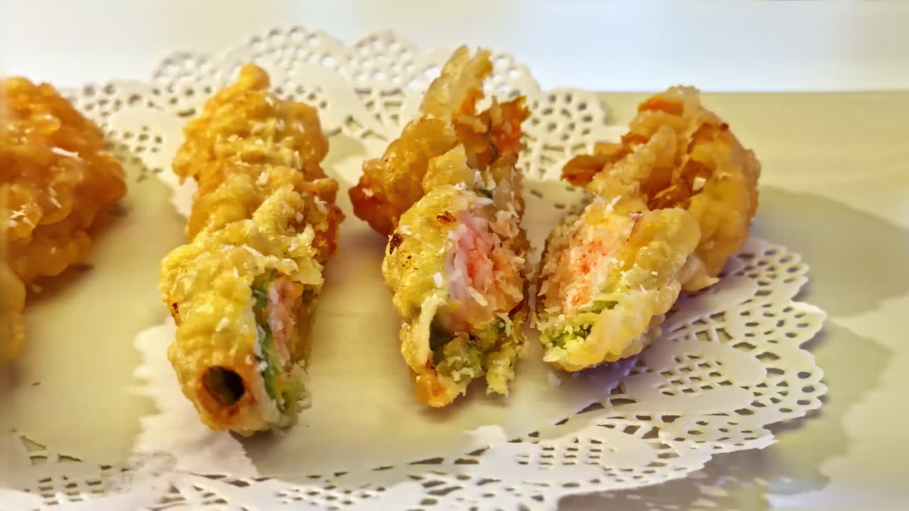 揚げたて天ぷら寿司ロールのクローズアップ映像。サクサクとした黄金色の衣と繊細な食感が特徴です。レストランで提供されるこの一皿は、カリカリとした外側と豊かな具材が際立っています。